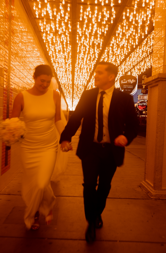 bride and groom running in downtown Las Vegas after their wedding. bride is wearing a white dress with a perfectly altered job and the groom a perfectly tailored suit.